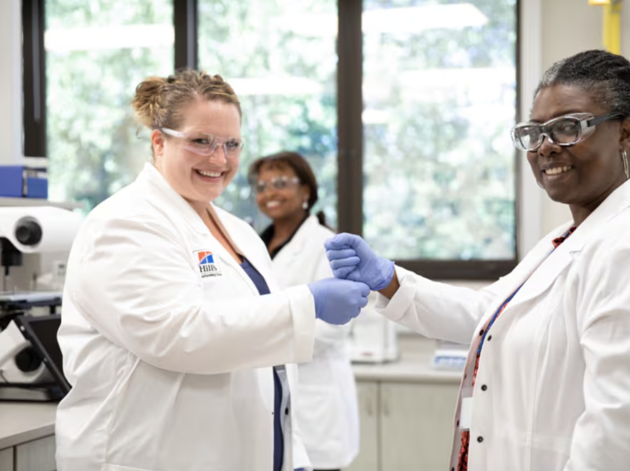Trois femmes souriantes, des scientifiques en blouses blanches et des lunettes de protection