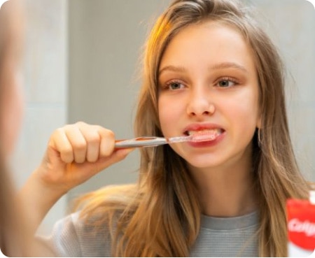 Une jeune fille se brossant les dents devant un miroir dans le cadre d'une routine d'hygiène dentaire saine.