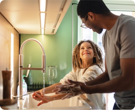 Un homme devant un évier de cuisine montrant à un enfant comment bien se laver les mains dans le cadre d'une routine d'hygiène saine.