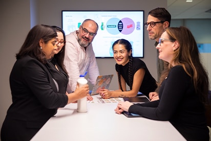 Six employés de Colgate-Palmolive dans une salle de réunion, en train de discuter d'un concept de produit, avec une diapositive de présentation projetée sur un écran derrière eux.