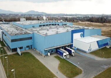 Suuri sininen logistiikkakeskus lintuperspektiivistä, jossa lastauslaitureilla on kuorma-autoja kuljetusta ja teollisuuden toimitusketjua varten.